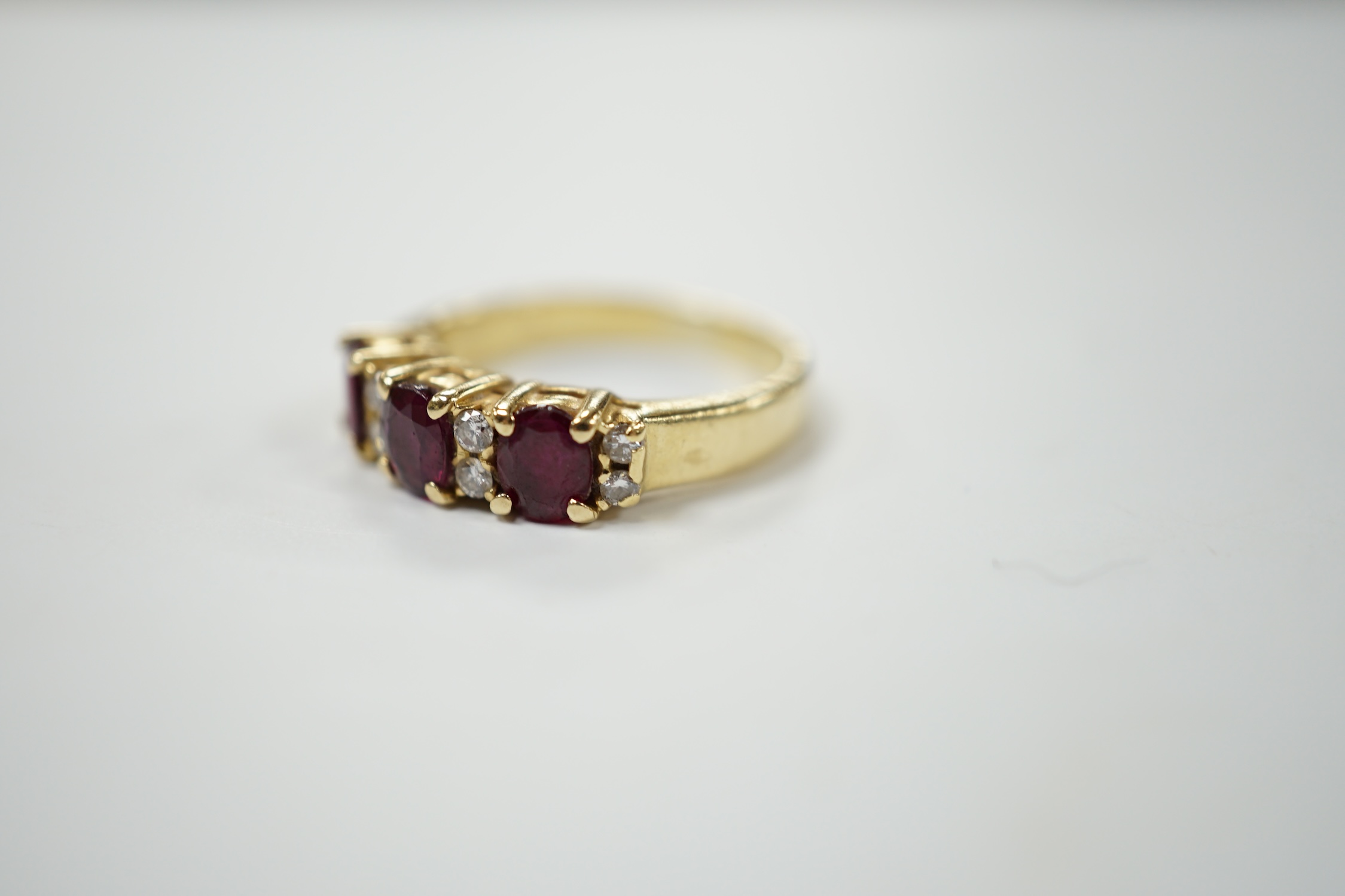 A modern yellow metal and three stone ruby set half hoop ring, with diamond chip spacers, size L, gross weight 5 grams. Condition - fair